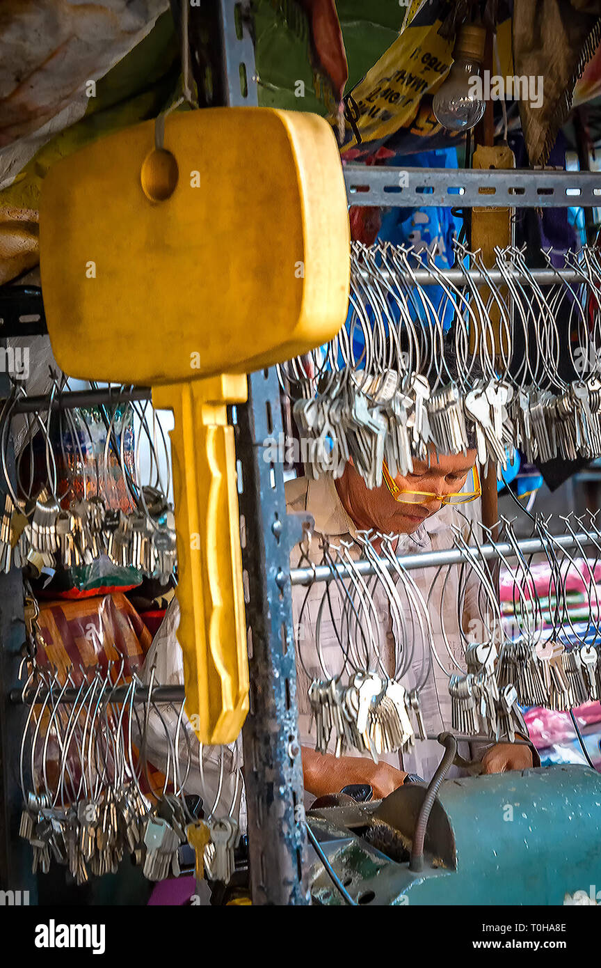 Samutsakorn, Tailandia - 14 Marzo 2019: un tasto strada smith duplica una chiave con la sua macchina per il taglio di chiavi. Egli sta lavorando dietro mazzi di chiavi appeso Foto Stock