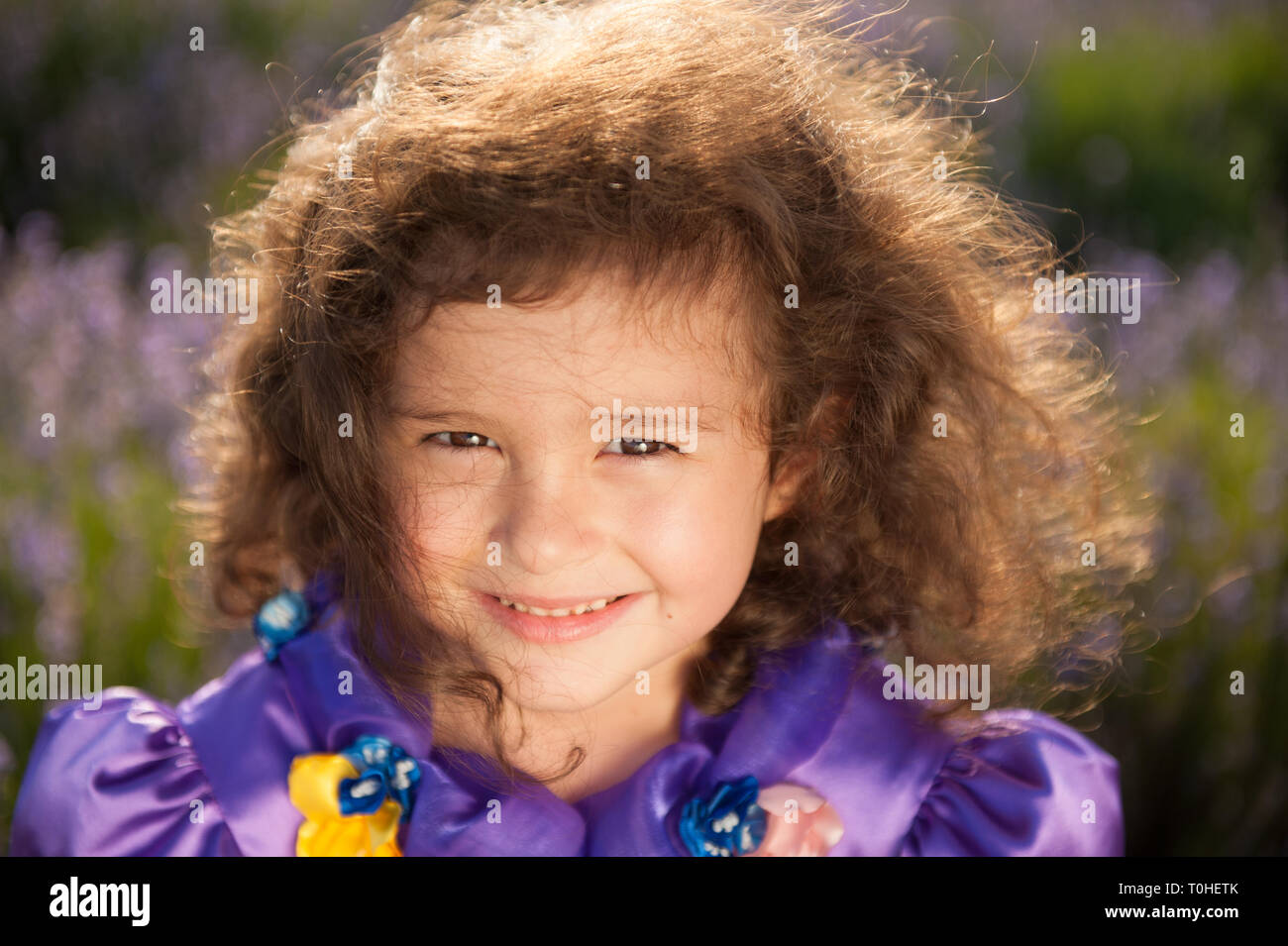 Ritratto di bella bambina indossa vestito viola con il vento nei capelli outdoor di campo dei fiori Foto Stock