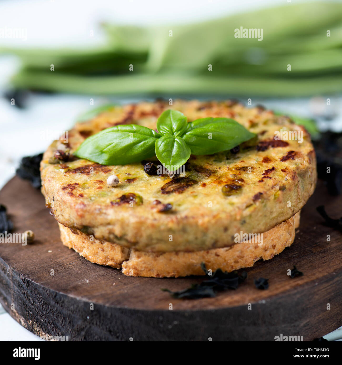 Primo piano di alcuni hamburger vegetariano, realizzato con fagiolini e altre verdure, su un round vassoio in legno, collocata su di un verde pallido tavola in legno rustico Foto Stock