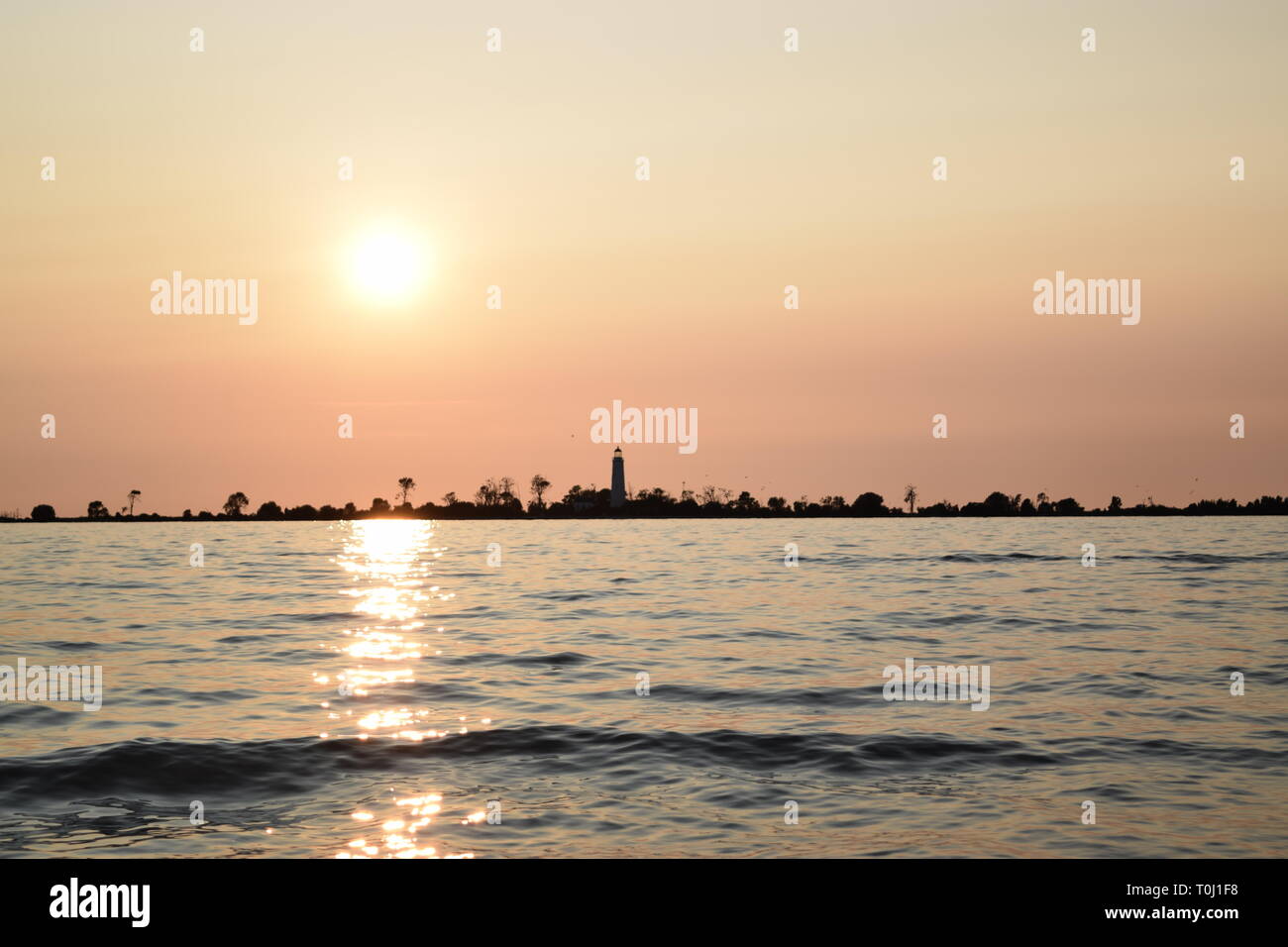 Tramonto sulla spiaggia con faro e acqua limpida. Liscia e tranquilla serata estiva, Ontario, Canada. Foto Stock