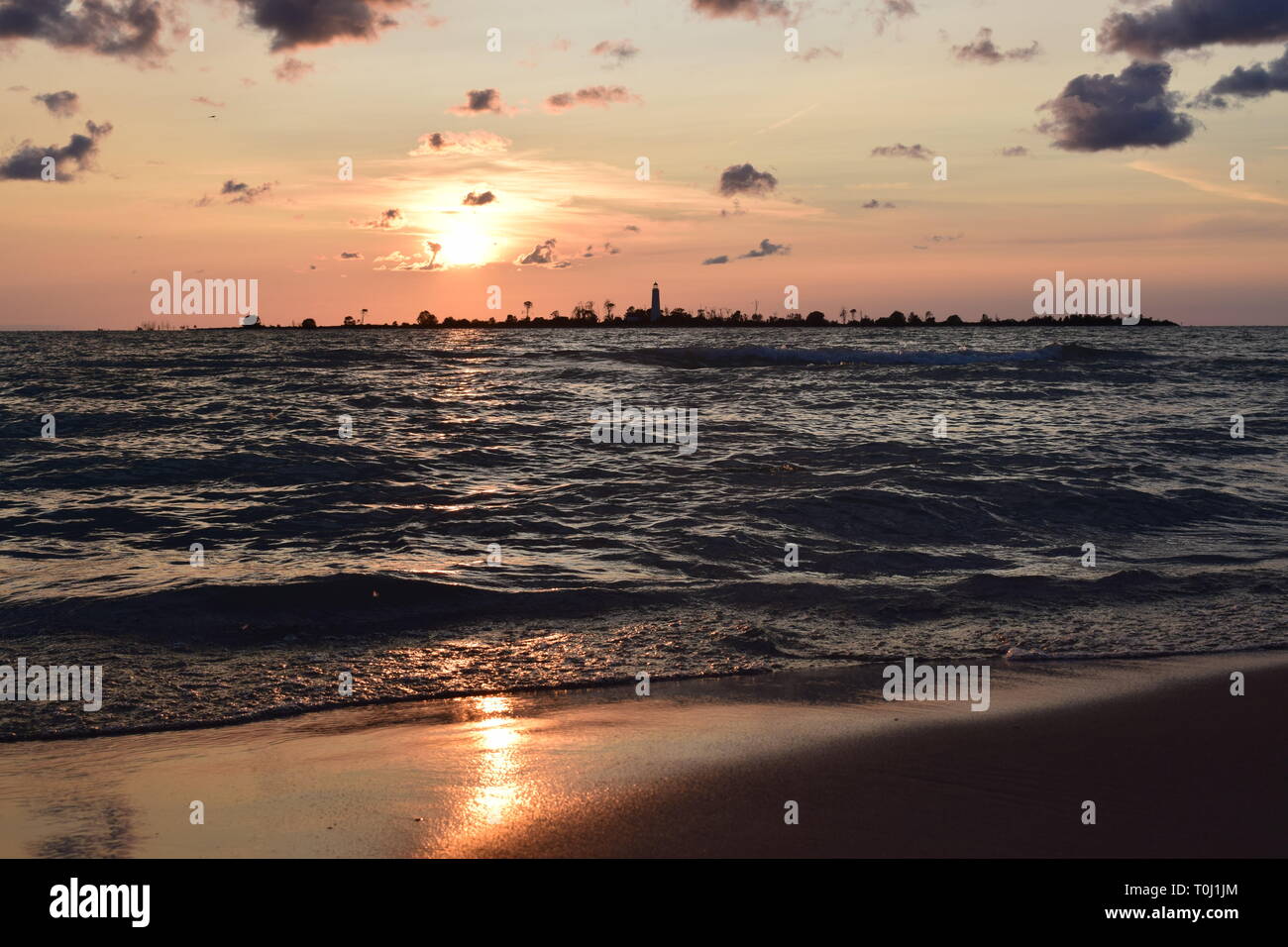 Tramonto sulla spiaggia con faro e acqua e macchie scure nuvole, ondulata, serata estiva, Ontario, Canada. Foto Stock