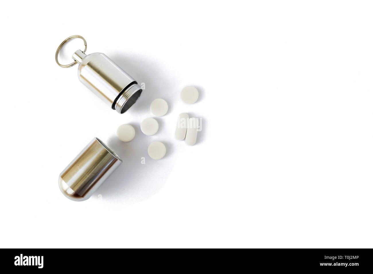 Medicina argento bottiglia con le pillole di bianco accanto ad essa, isolato su sfondo bianco. Portable chiave catena contenitore per pillole e piccoli oggetti utili per h Foto Stock