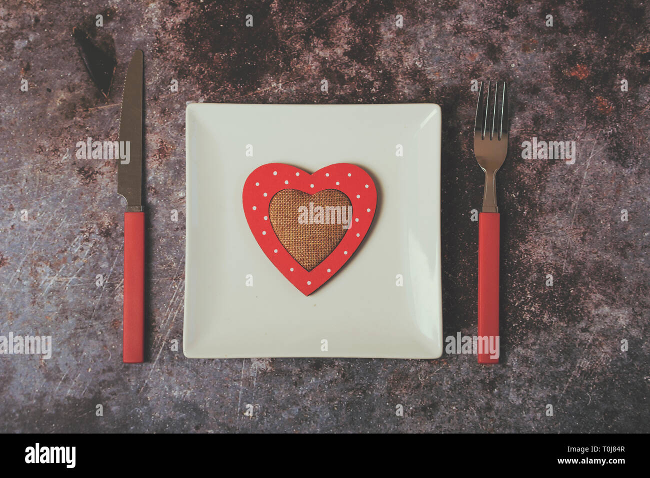 Cuore rosso su una piastra bianca accanto a posate contro sfondo Grunge Foto Stock