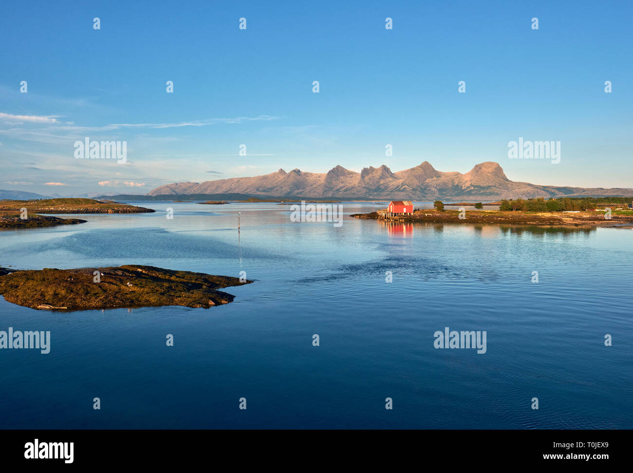 Un rosso rorbuer house e la fascia costiera che si affaccia De Syv søstre / Le sette sorelle mountain range sull isola di Alsten Alstahaug Nordland, Norvegia Foto Stock