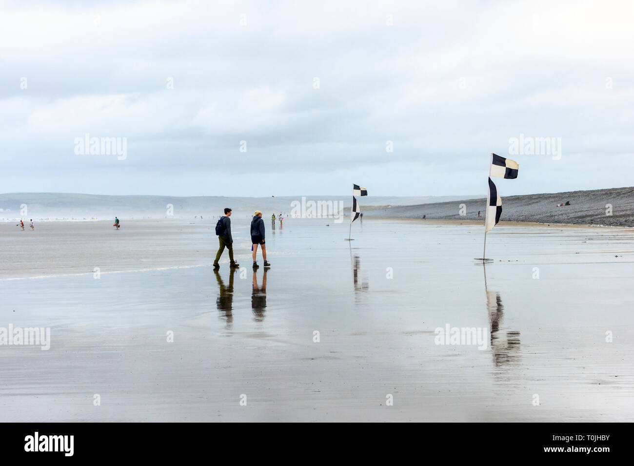 I villeggianti camminando sul ventoso spiaggia sabbiosa a Condino, Devon, Regno Unito, su un nuvoloso e ventoso mattinata estiva Foto Stock