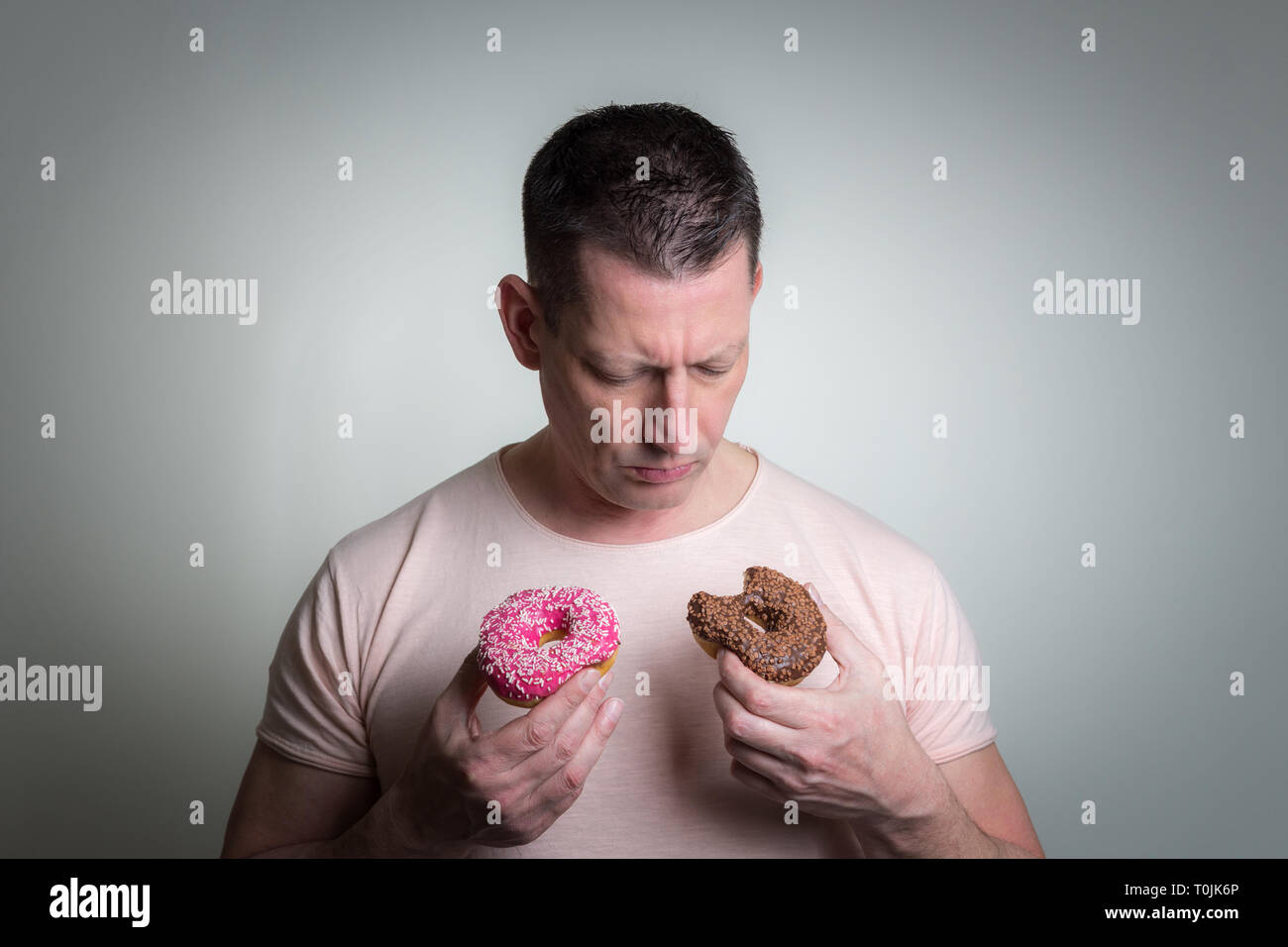 Uomo caucasico con marrone e ciambelle rosa su sfondo grigio Foto Stock