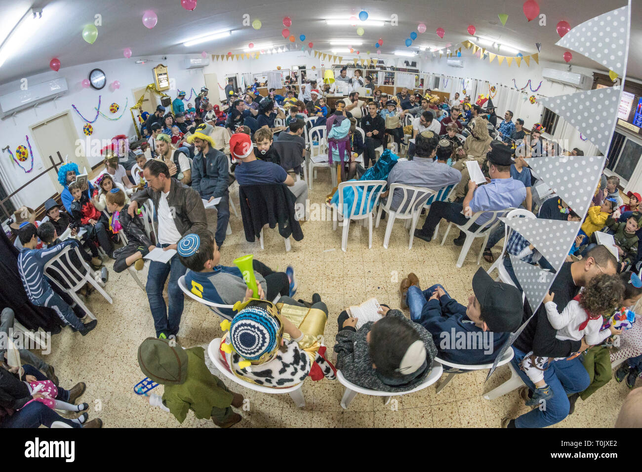 Elkana, Israele. 20 Mar, 2019. Le persone e i bambini in una sinagoga nel villaggio israeliano di Elkana durante la lettura del libro di Ester in una Sinagoga durante la festa ebraica di Purim. In questa vacanza ebrei traditionaly vestito in costumi, leggere la chiocciola di Esther, una storia su un anti-ebraica complotto fallito nell antica Persia e fare un racket ogni volta che il nome di Haman, l'antagonista principale, è menzionato. Credito: Yagil Henkin/Alamy Live News Foto Stock