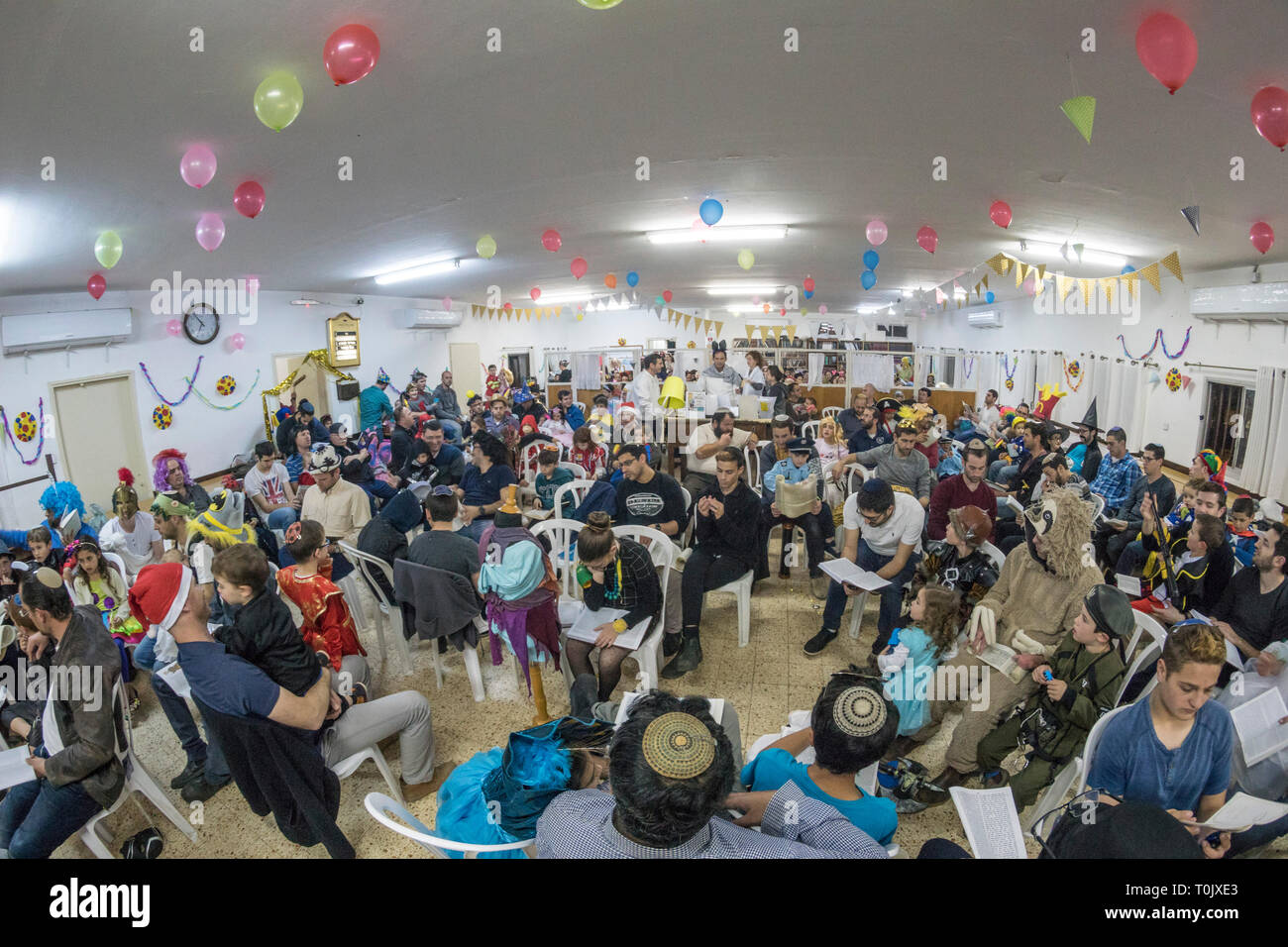 Elkana, Israele. 20 Mar, 2019. Le persone e i bambini in una sinagoga nel villaggio israeliano di Elkana durante la lettura del libro di Ester in una Sinagoga durante la festa ebraica di Purim. In questa vacanza ebrei traditionaly vestito in costumi, leggere la chiocciola di Esther, una storia su un anti-ebraica complotto fallito nell antica Persia e fare un racket ogni volta che il nome di Haman, l'antagonista principale, è menzionato. Credito: Yagil Henkin/Alamy Live News Foto Stock