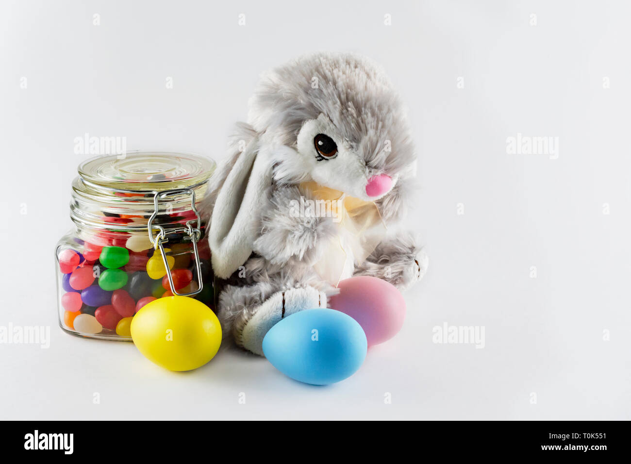 Giocattolo imbottito coniglietto di pasqua con tinte colorate le uova e un vaso di vetro riempito con Jelly Beans su uno sfondo bianco. Spazio di copia a destra. Foto Stock