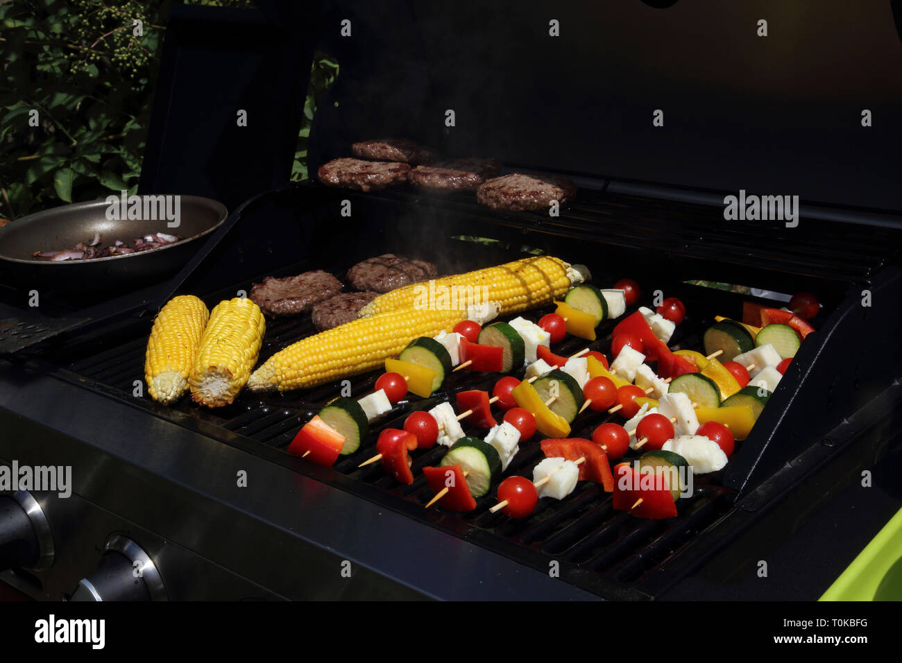 Per la cottura di spiedini, sulla pannocchia di mais e gli hamburger sul barbecue nel giardino Gillingham Dorset Inghilterra Foto Stock