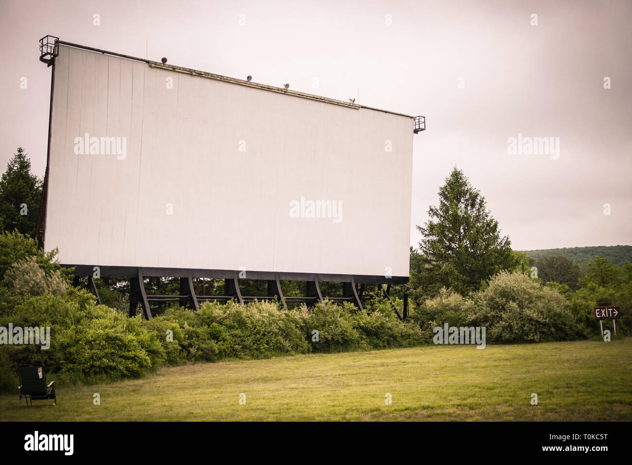 Drive-in theatre schermata film sorge nella distanza; circondato da erba e boschivo overgrowth. Foto Stock