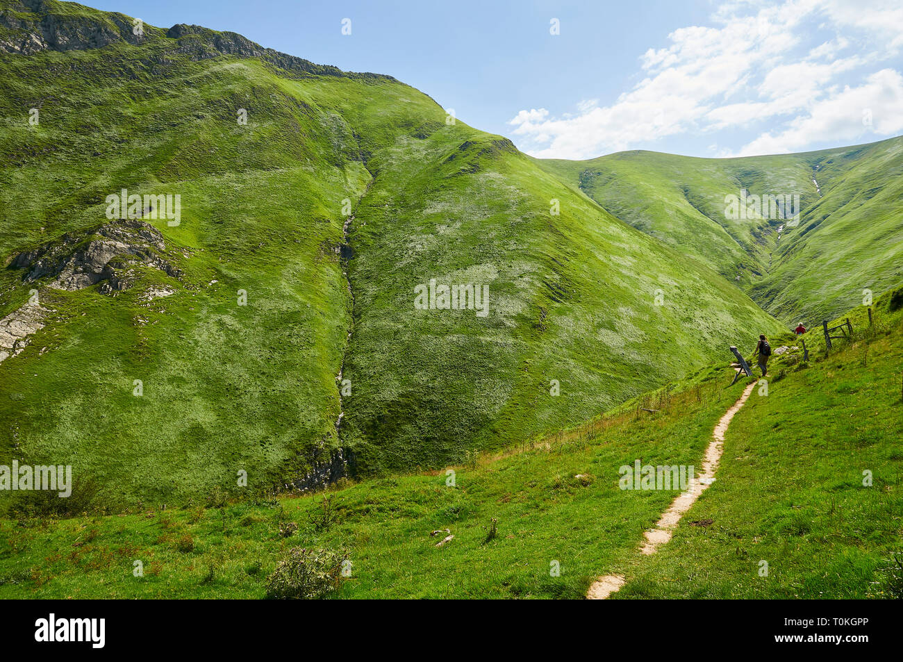 Giovane donna escursionismo in il sentiero alla grotta Arpea, spettacolare piega anticlinale piega circondato da verdi pascoli nei Pirenei francesi (Estérençuby, Francia) Foto Stock