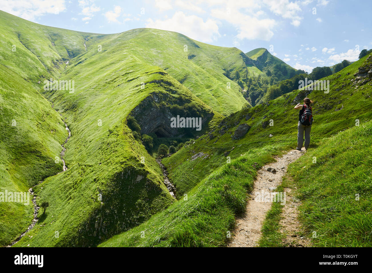 Giovane donna in una scia di fotografare Arpea grotta, spettacolare piega anticlinale piega circondato da verdi pascoli nei Pirenei francesi (Estérençuby, Francia) Foto Stock