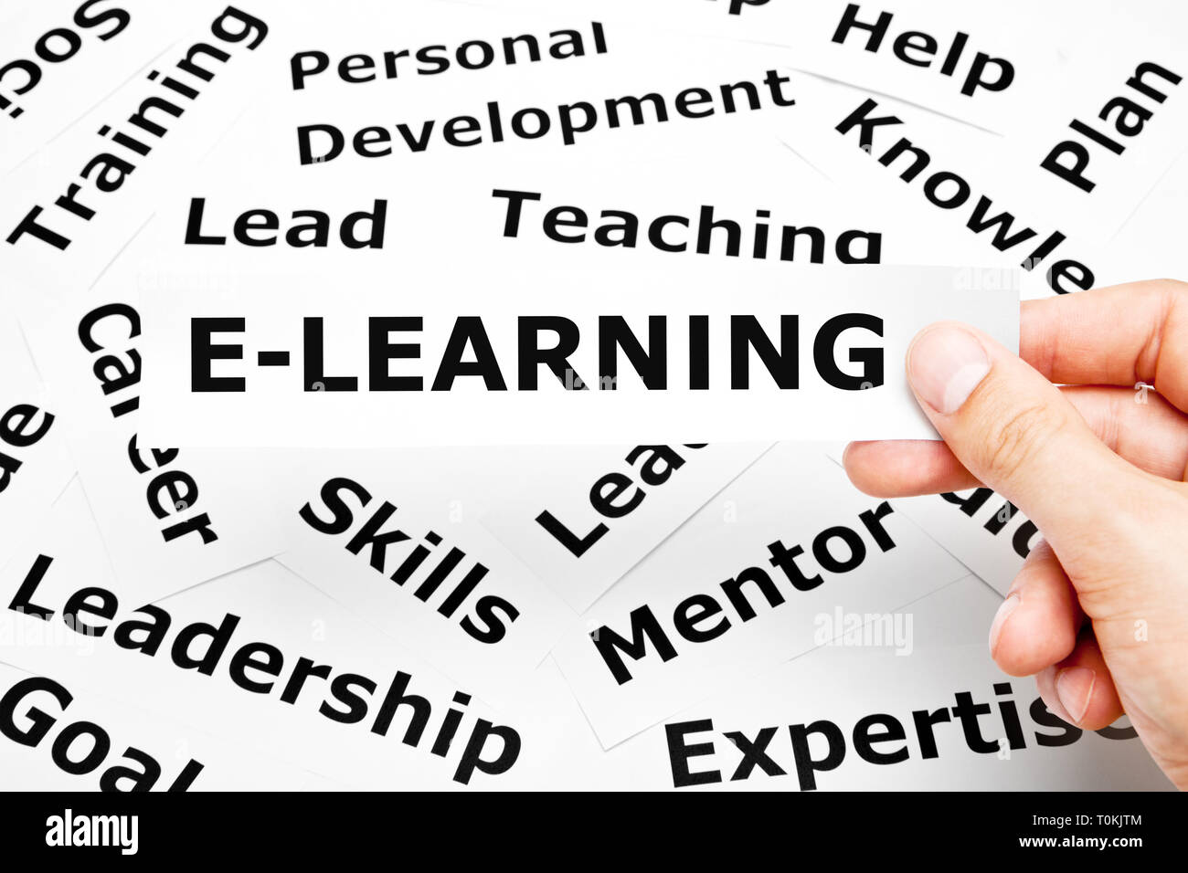 Mano che tiene un pezzo di carta con la parola E-Learning stampati su di essa al di sopra di altre parole correlate sullo sfondo. Foto Stock