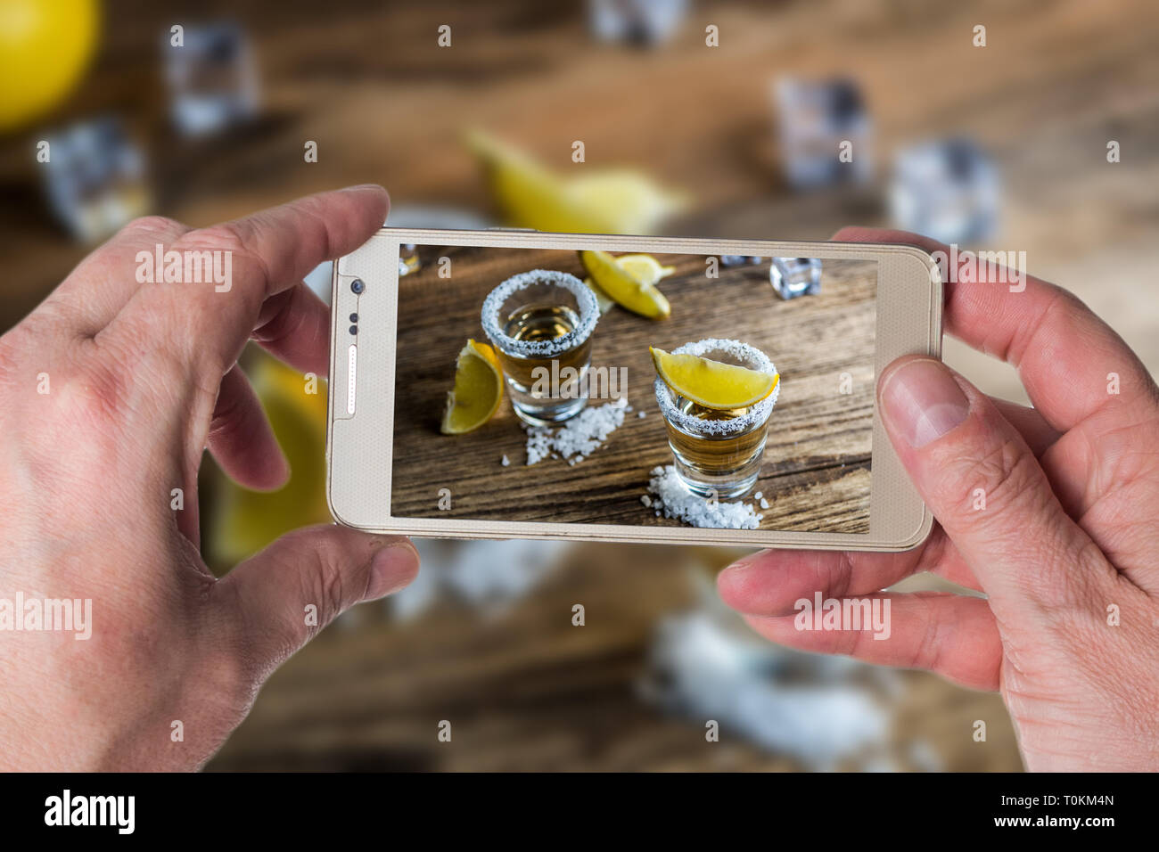 L'uomo prendendo foto del tradizionale messicano alcool bere la tequila con limone e sale e cubo di ghiaccio sul tavolo di legno Foto Stock