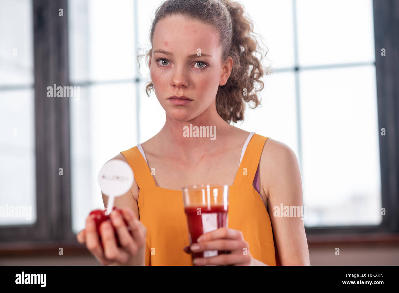 La donna in giallo brillante portante superiore mini pomodori e bicchiere pieno con succo Foto Stock