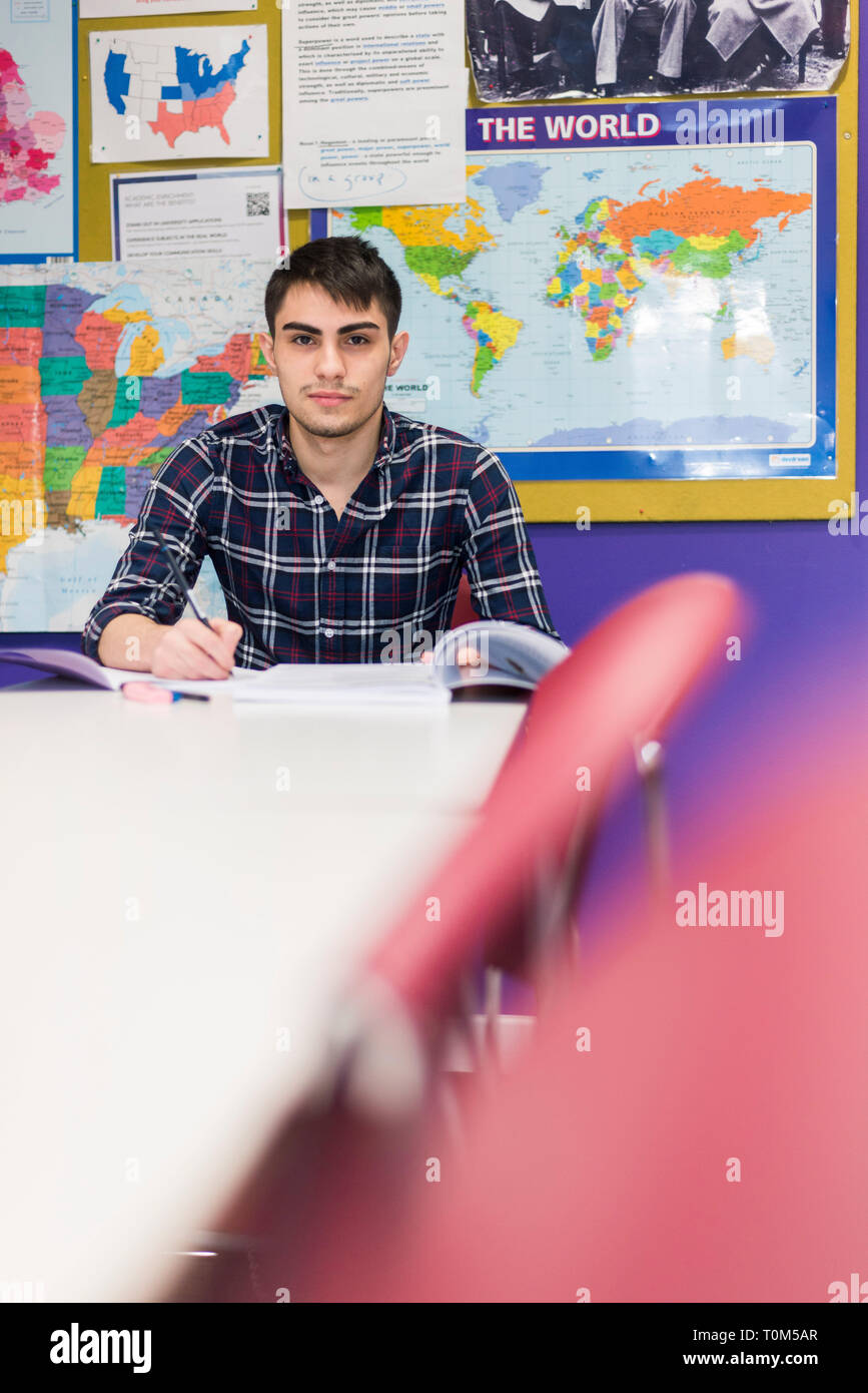 Un giovane medio orientale studente si siede a un tavolo durante una lezione e scrive delle note Foto Stock