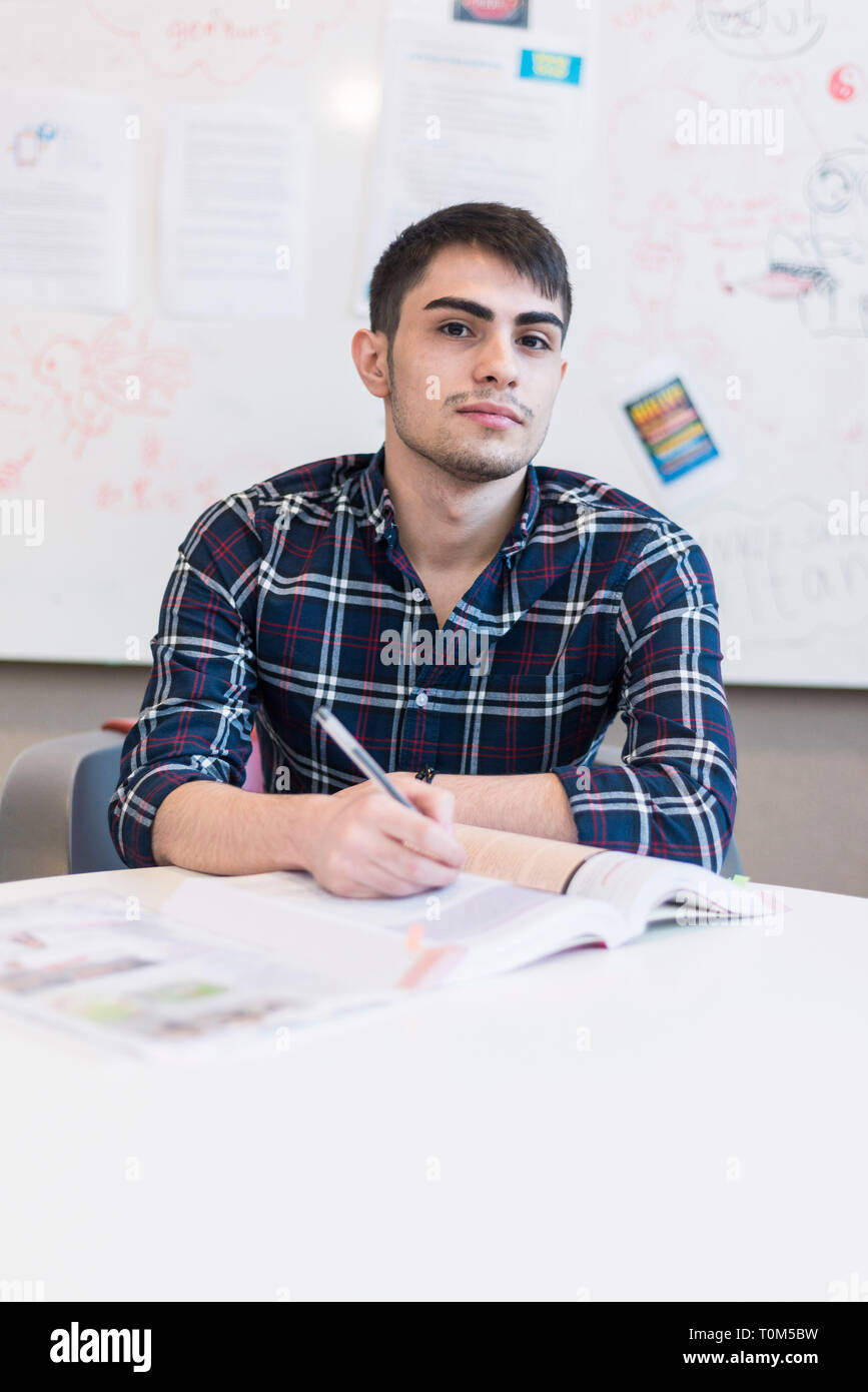 Un giovane medio orientale studente si siede a un tavolo durante una lezione e scrive delle note Foto Stock