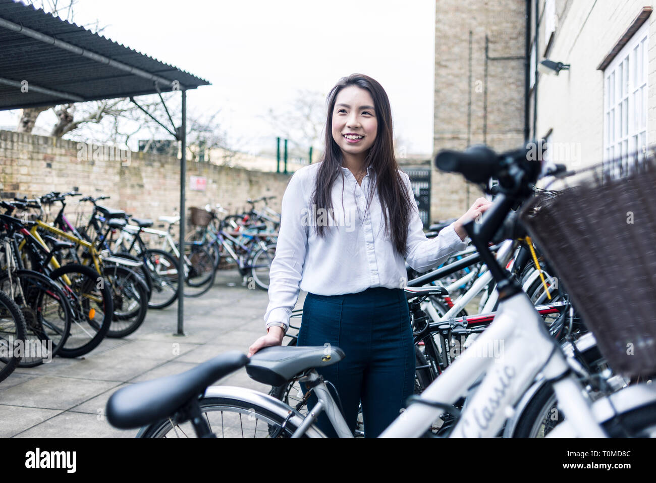 Uno studente internazionale si erge tra il deposito bici e molte biciclette Foto Stock