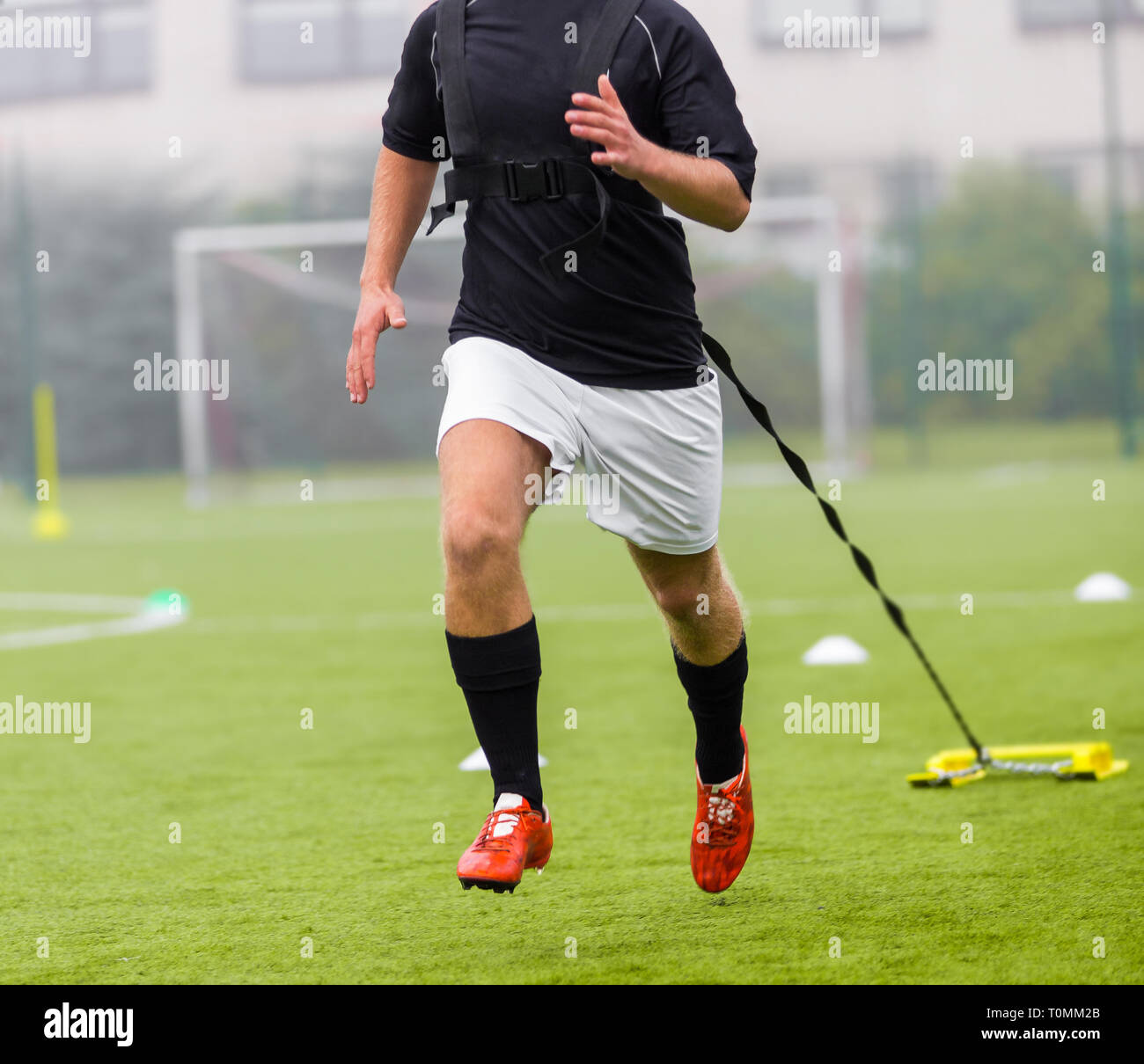 Giocatore di calcio viene eseguito durante il trascinamento di pesi dietro di lui. Esecuzione con pesi allenamento per il calcio. Trascinare il calcio pratica di allenamento Foto Stock