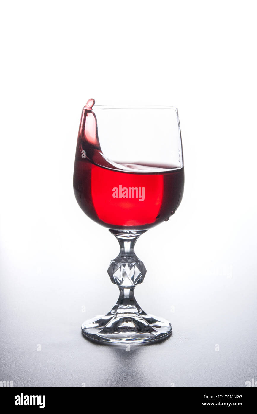 Bibite e bevande concezione. Il vino rosso di spruzzi di vino in vetro con gocce di dinamica su sfondo chiaro. Foto Stock