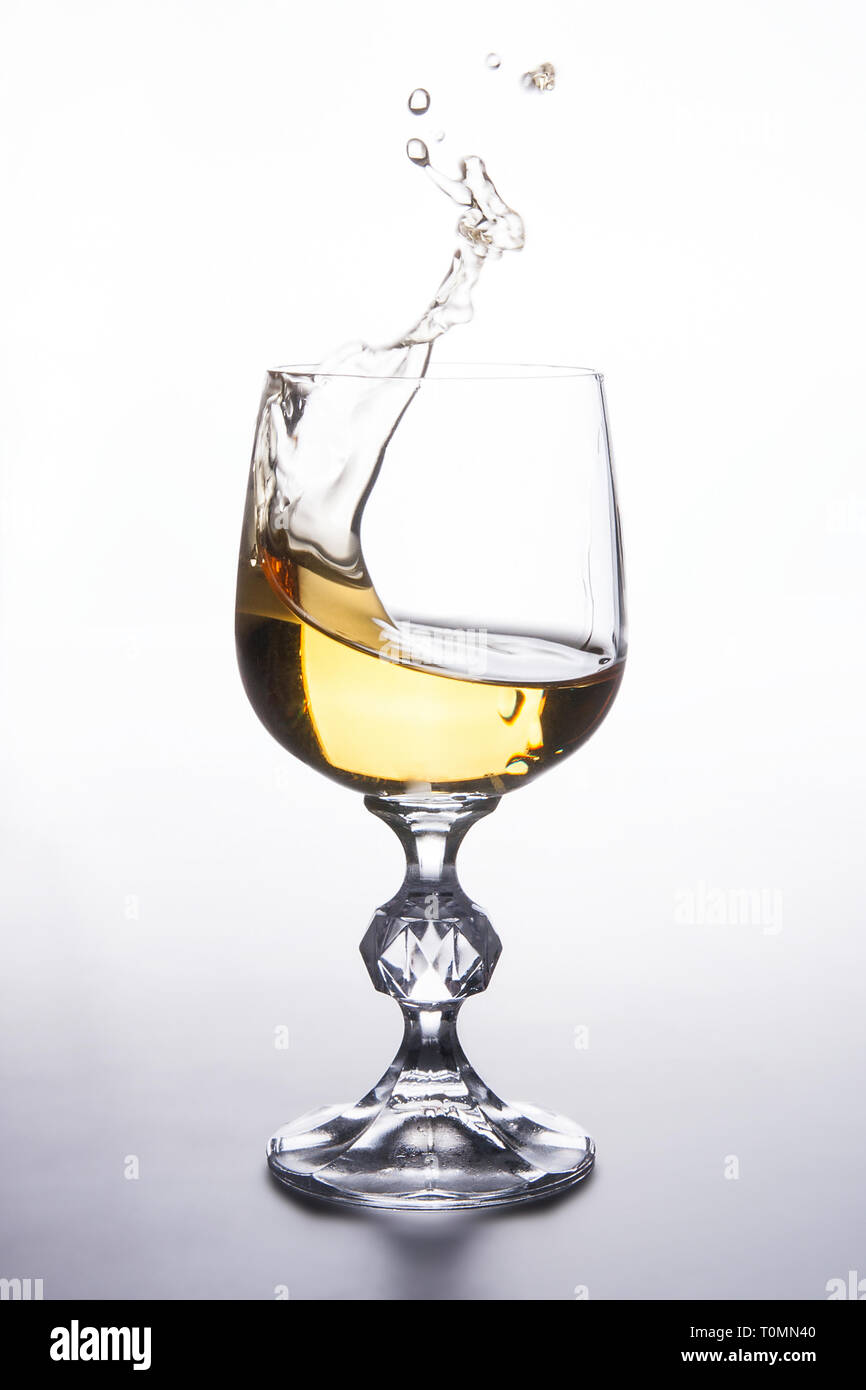 Bibite e bevande concezione. Vino bianco di spruzzi di vino in vetro con gocce di dinamica su sfondo chiaro. Foto Stock