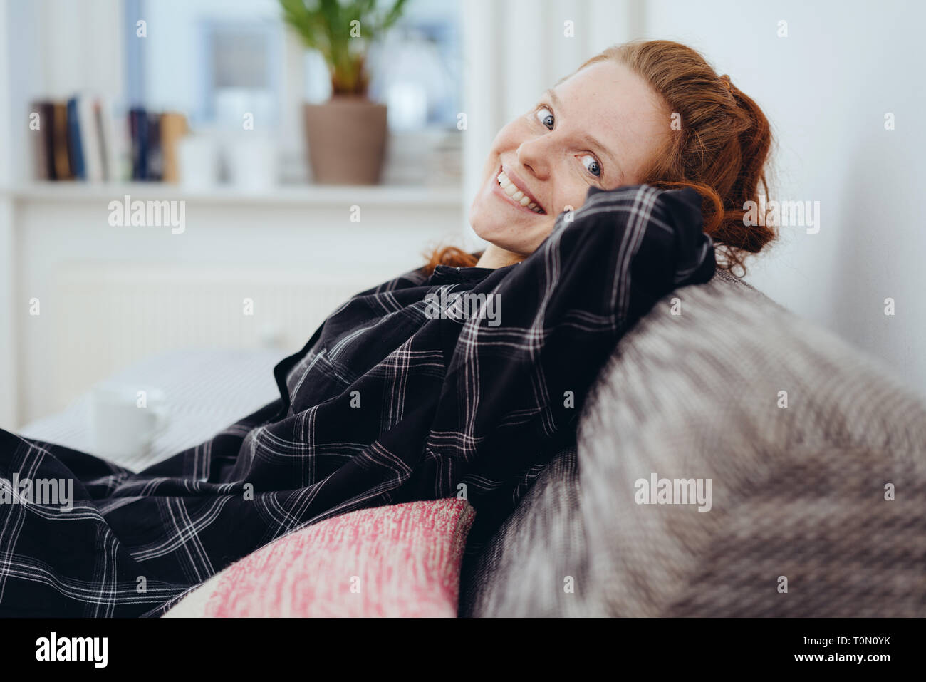 Felice gentile giovane donna redhead relax su un divano svolta a guardare la fotocamera con un bel sorriso caldo Foto Stock