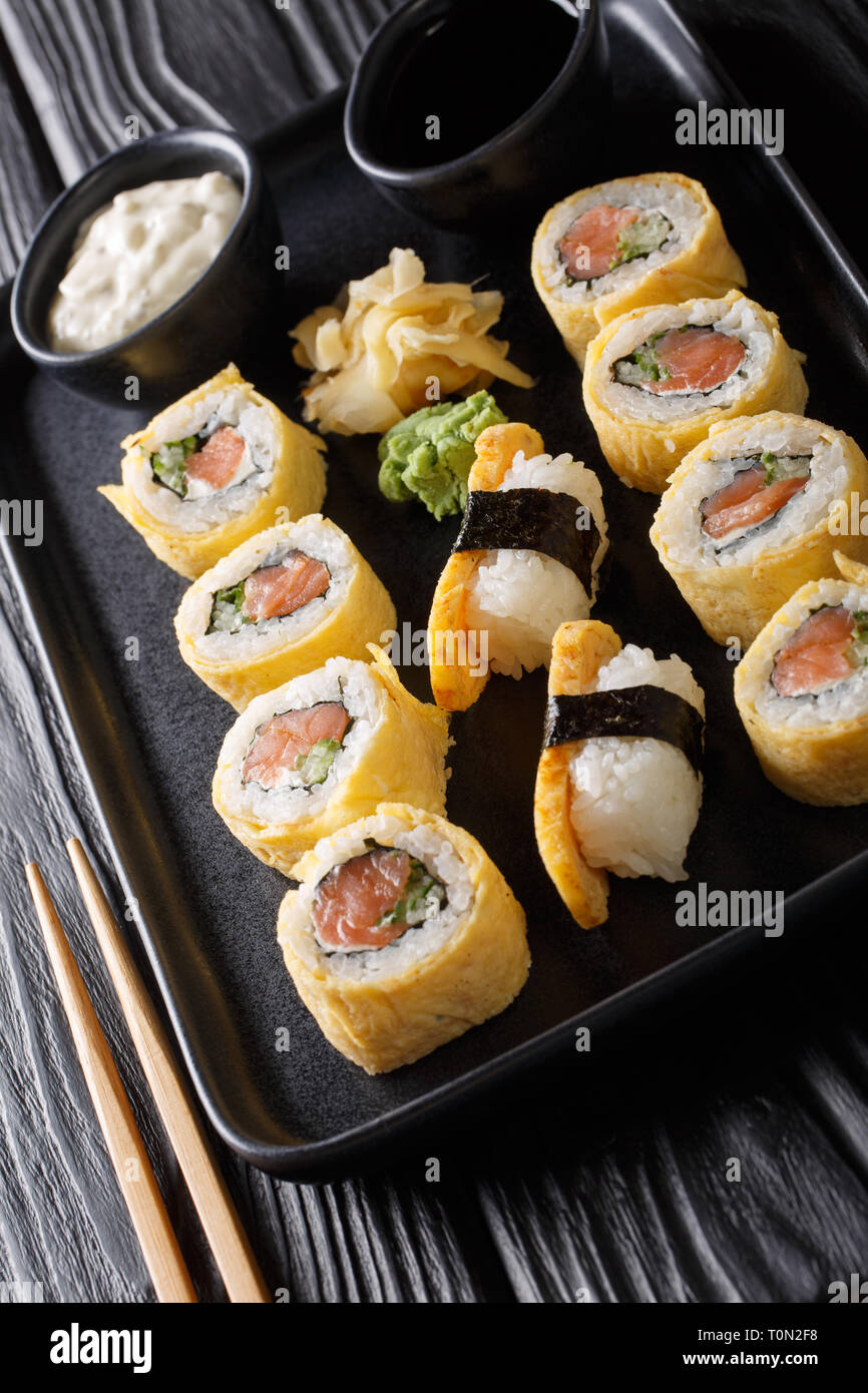 Impostare tamagoyaki rotolo di sushi con riso, formaggio, salmone e avocado closeup su una piastra sul piano verticale. Foto Stock
