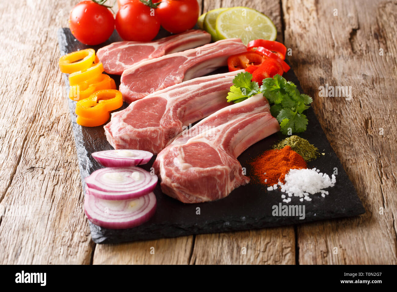 Set di alimenti crudi per la cottura di costolette di agnello con verdure fresche e spezie close-up su una scheda di ardesia sul tavolo. Posizione orizzontale Foto Stock