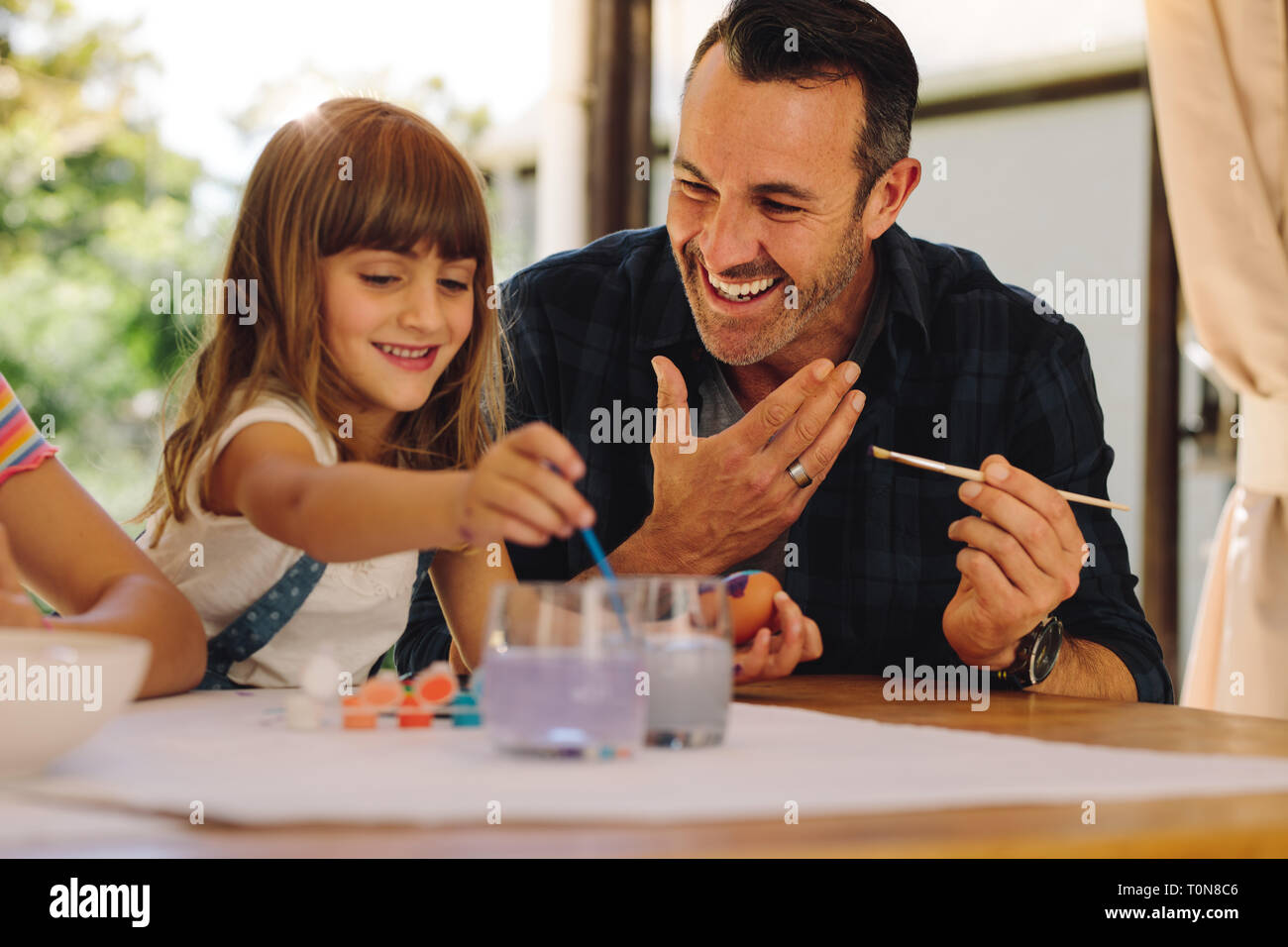 Padre e figlia di pittura delle uova di pasqua insieme. Uomo sorridente aiutare sua figlia dipingere uova di pasqua. Foto Stock