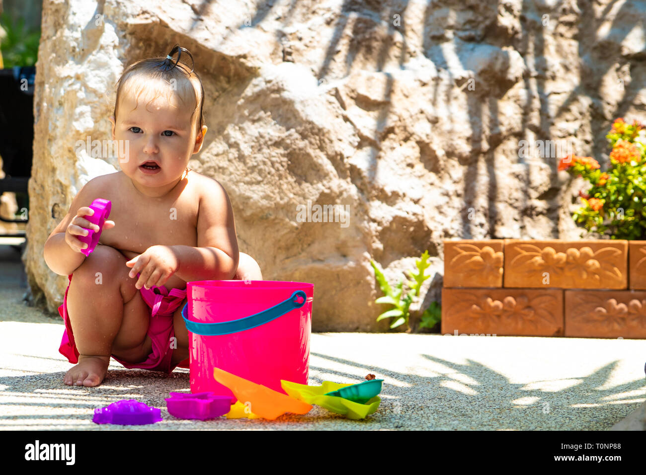 Un anno di età ragazza in un rosa costume gioca con giocattoli da spiaggia. Foto Stock