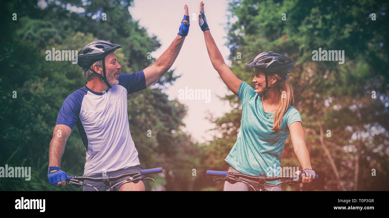 Atletica Giovane dando alta cinque mentre equitazione bicicletta su strada Foto Stock
