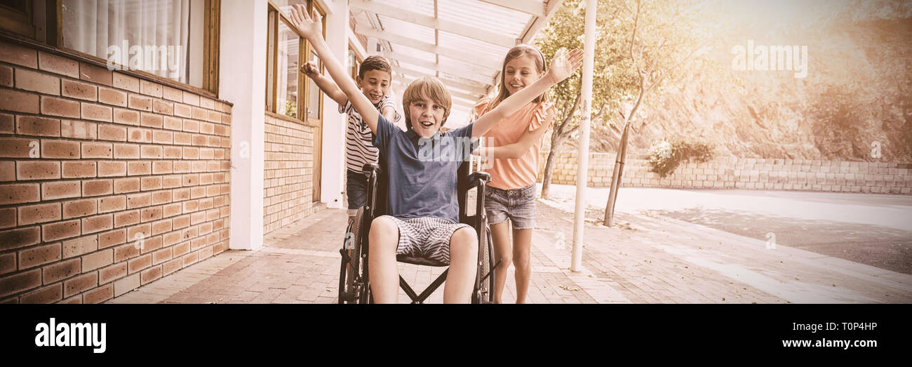 Ragazzi delle scuole spingendo un ragazzo su una sedia a rotelle Foto Stock