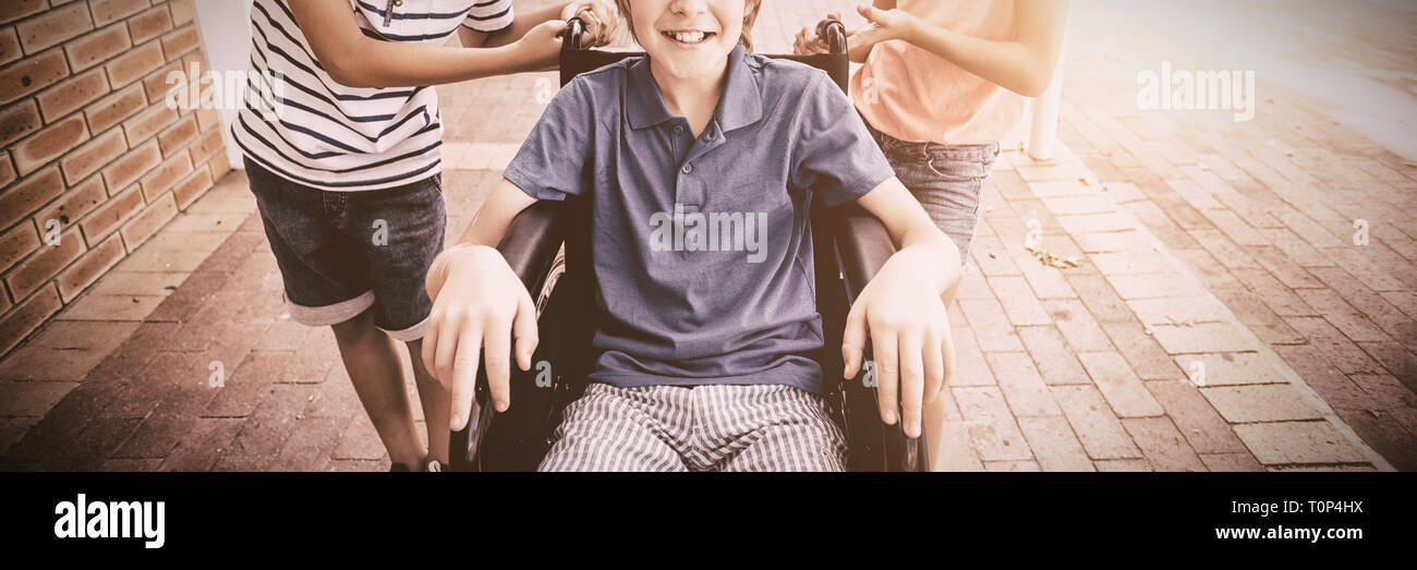 Ragazzi delle scuole spingendo un ragazzo su una sedia a rotelle Foto Stock