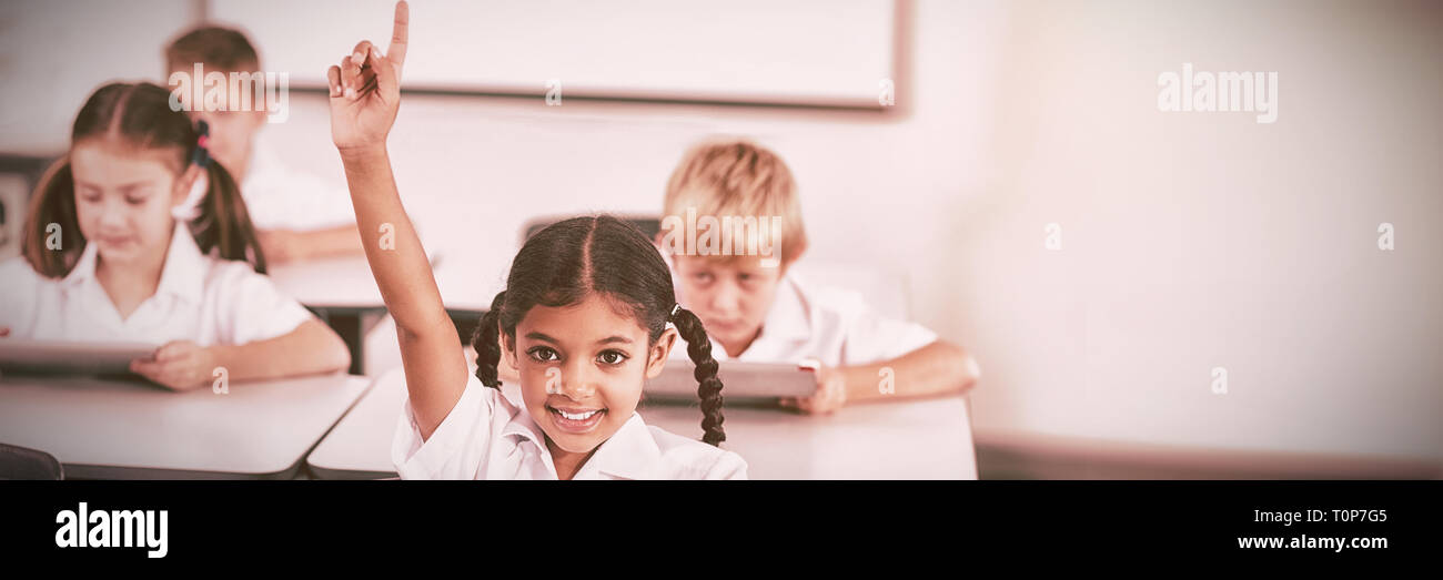 Sorridente schoolgirl alzando la mano in aula Foto Stock