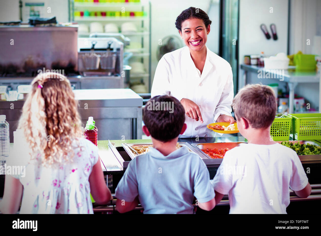 Allegra donna che serve cibo agli allievi delle scuole Foto Stock