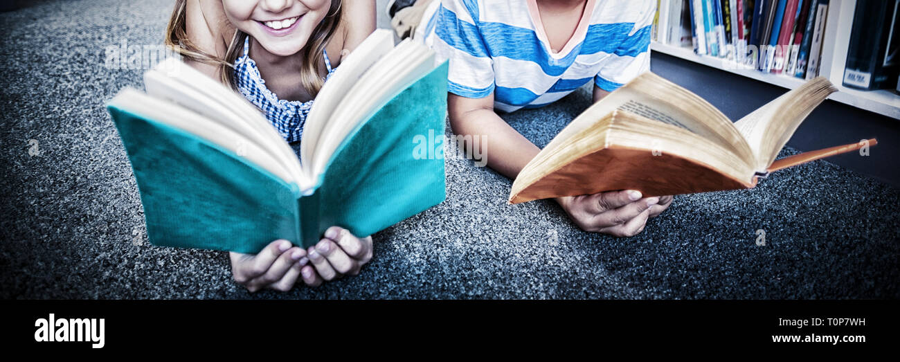 Felici i bambini della scuola sdraiato sul pavimento e la lettura di un libro in biblioteca Foto Stock