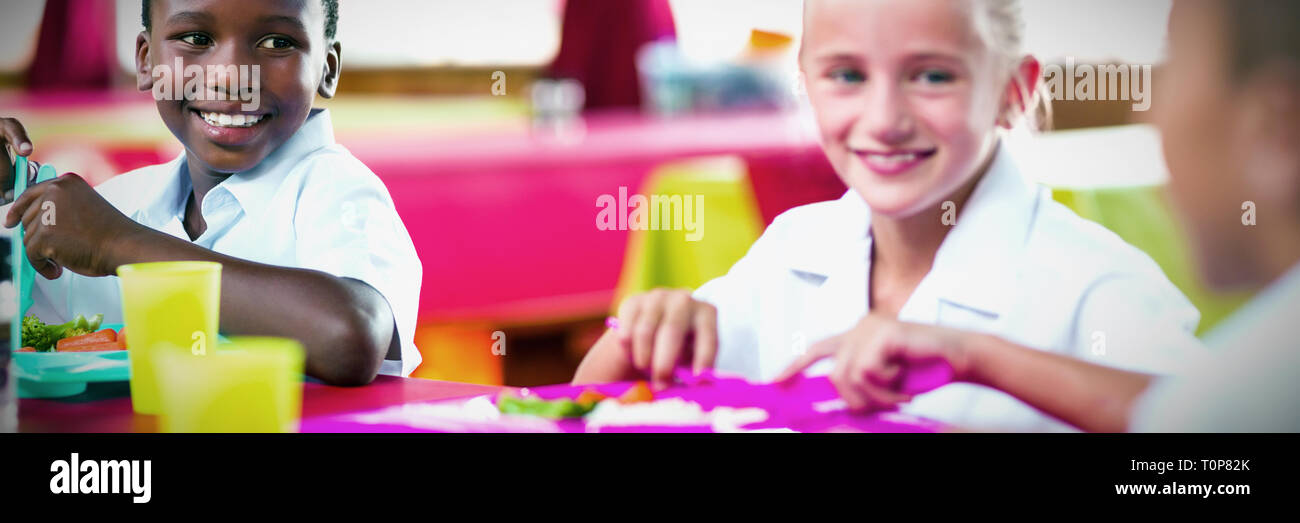 Bambini aventi il pranzo durante il tempo di interruzione in mensa scolastica Foto Stock