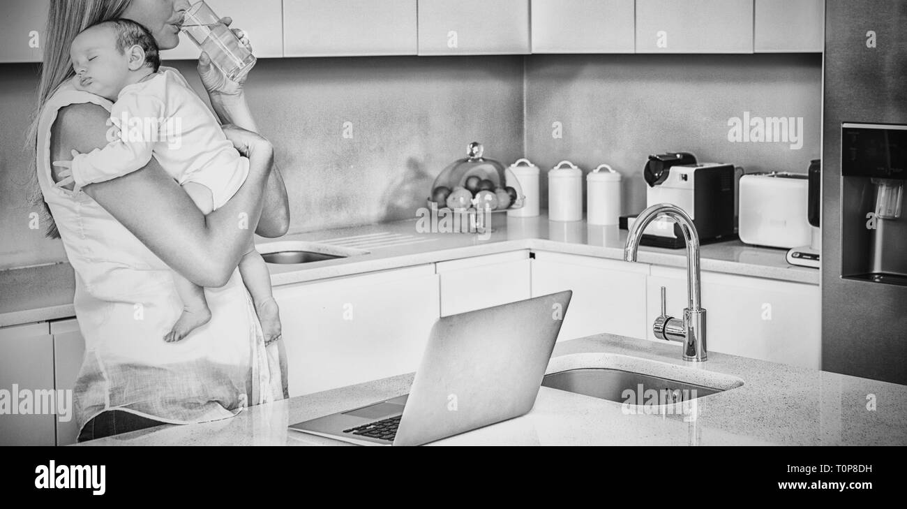 Giovane donna acqua potabile mentre il bambino portando in cucina Foto Stock