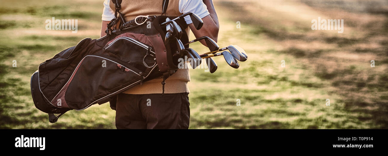 Uomo che porta sacca da golf mentre si sta in piedi sul campo Foto Stock