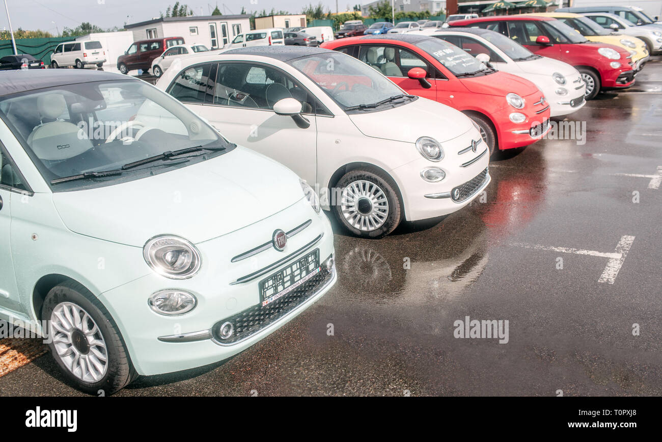 Immagine della piccola e bella Fiat Auto in piedi fuori sul parcheggio. Ci sono il bianco e il rosso auto. Asfalto bagnato sotto le ruote Foto Stock
