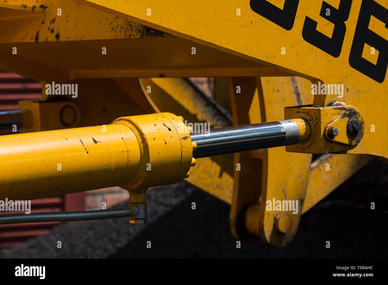 Shiny asta del cilindro idraulico e di altri meccanismi di giallo macchine stradali, colorate con bitume, close-up su uno sfondo sfocato Foto Stock