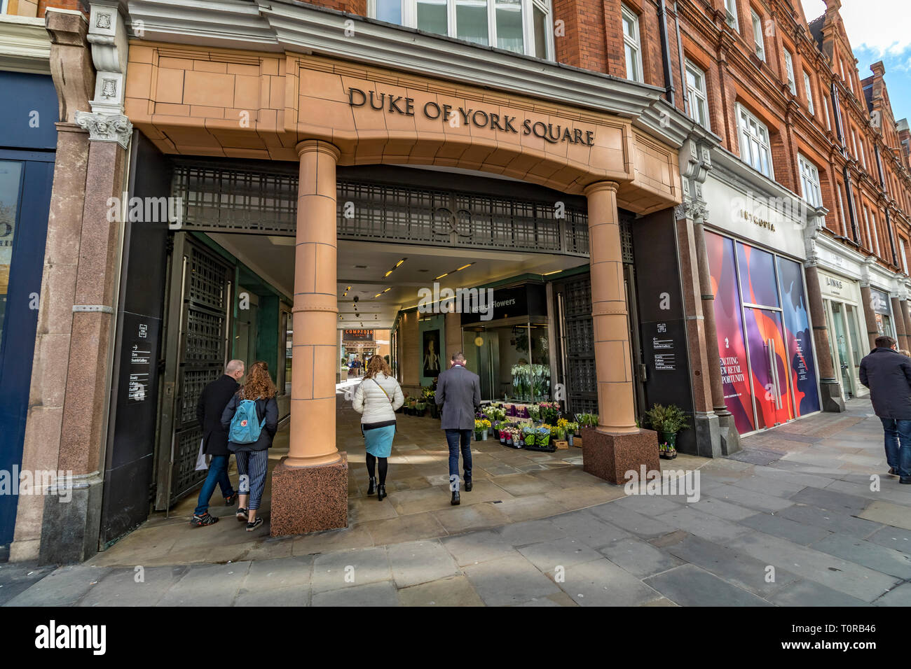 Persone che camminano attraverso l'entrata a Duke of York Square, Sloane Square, Chelsea, Londra, Regno Unito Foto Stock