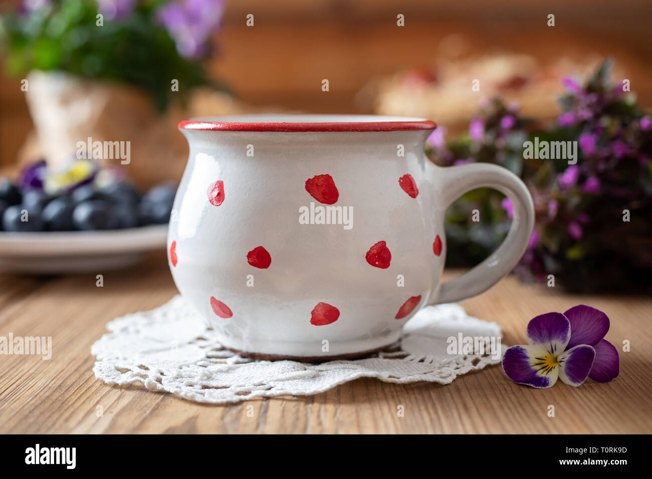 Polka Dot mug su un tavolo, con viola dead-ortiche, pansies e mirtilli in background Foto Stock