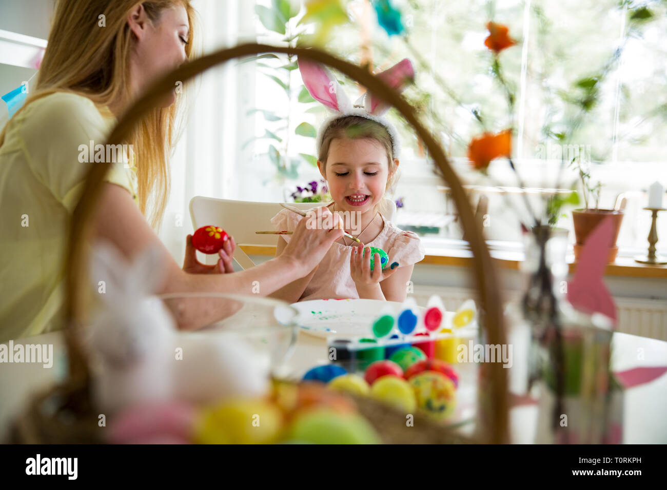 Una madre e figlia che celebrano la pasqua pittura delle uova con la spazzola. Carino bambina nelle orecchie di coniglietto preparare la vacanza. Foto Stock