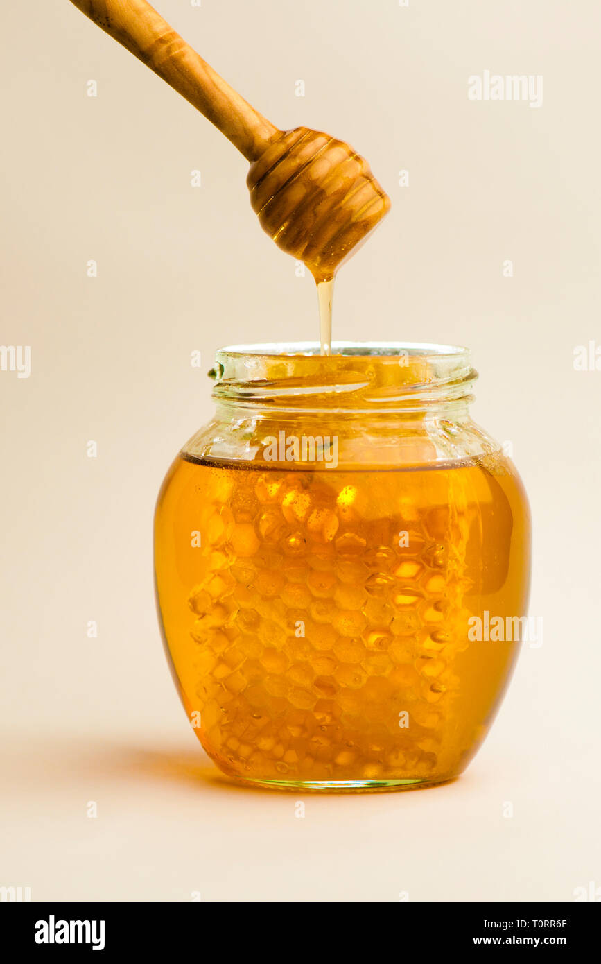 Vaso di miele di favo di miele e bilanciere in legno contro uno sfondo semplice Foto Stock