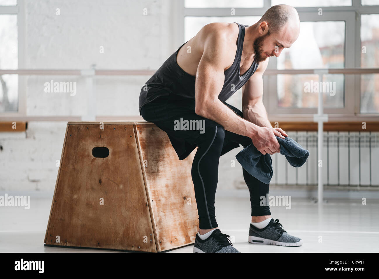 Muscoloso uomo seduto con asciugamano sulla casella in palestra. Atleta  maschio relax dopo il suo intenso allenamento presso la sala a croce Foto  stock - Alamy