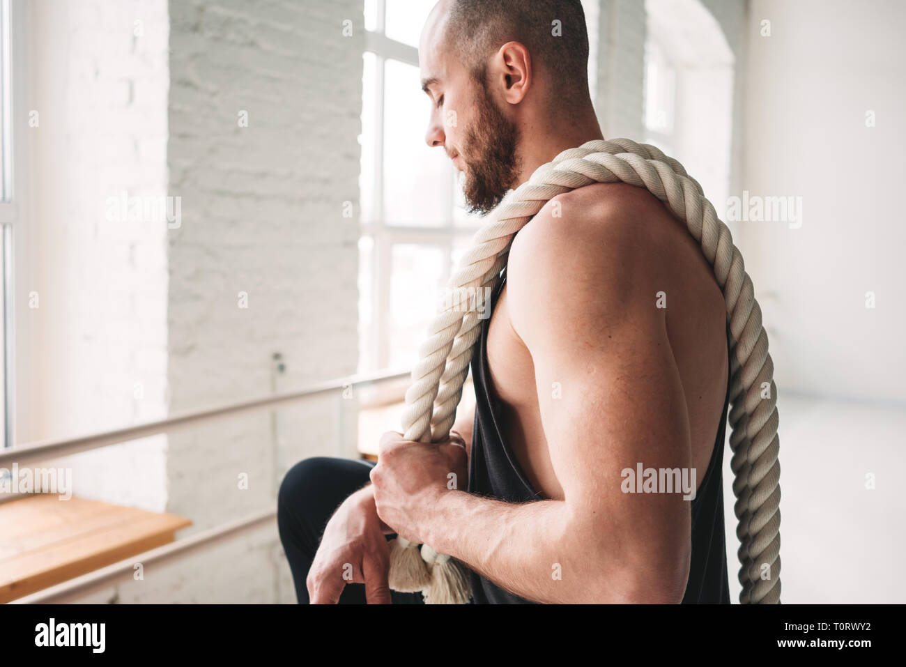 Bel uomo muscolare tenendo sullo spallamento corda allenamento in palestra di luce. Ritratto di uomo fitness con funi di battaglia a croce palestra Foto Stock