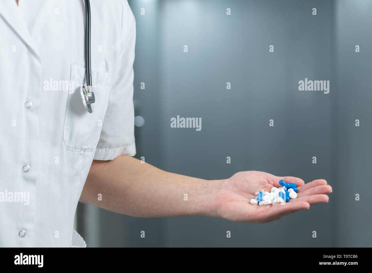 Luminose ravvicinata di un medico di sesso maschile in uniforme con uno stetoscopio e holding del bianco e del blu pillole in una mano Foto Stock
