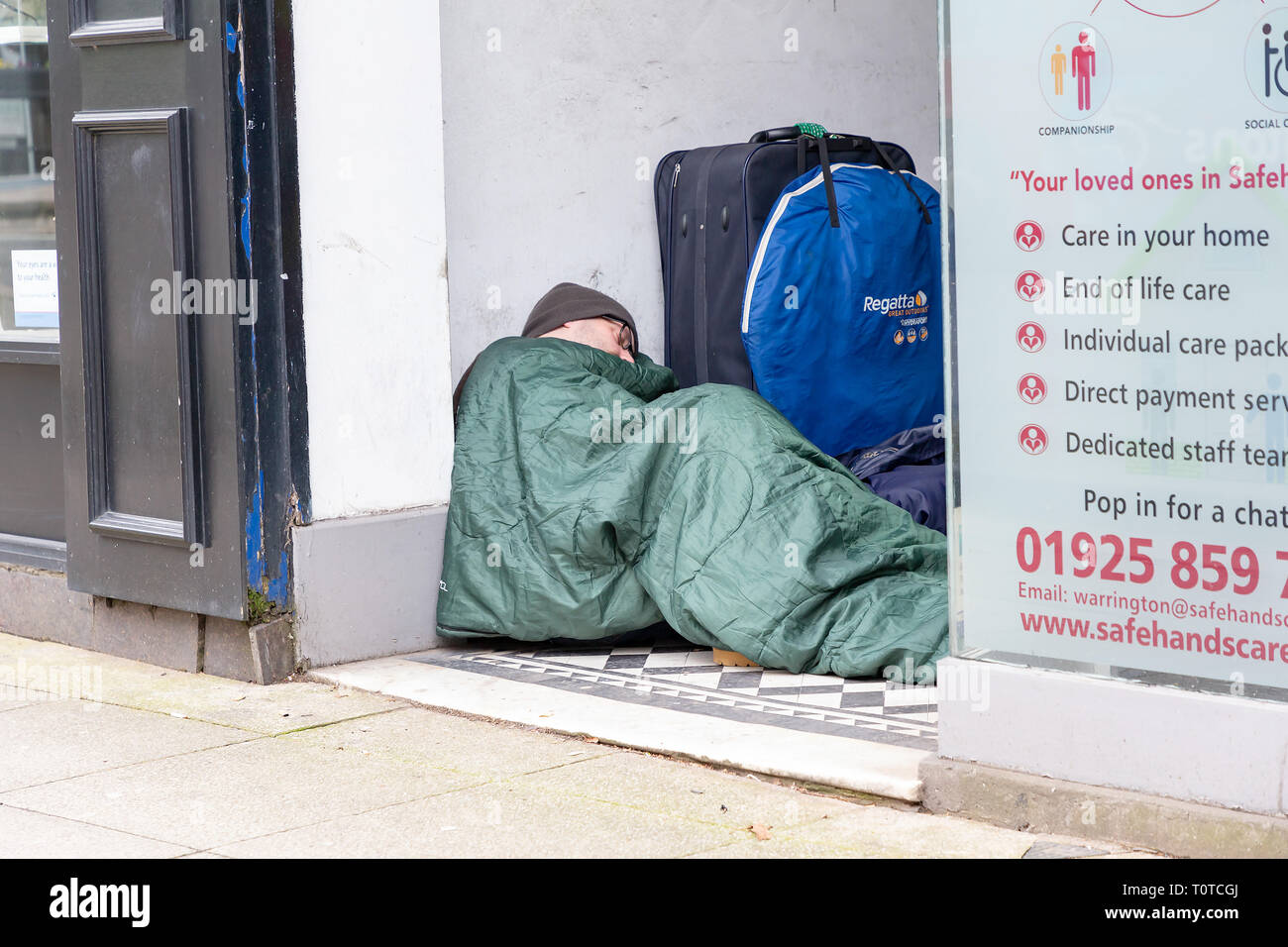 Senzatetto uomo dorme in modo irregolare a un negozio che porta in centro citta' di Warrington, Cheshire, Regno Unito Foto Stock